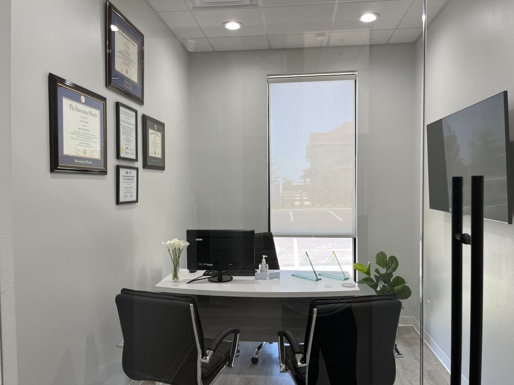 Consultation office in Magnolia Dental with a desk, chairs, and framed certificates on the wall.